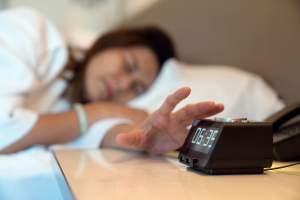 Image of woman pressing the stop button on her alarm clock.