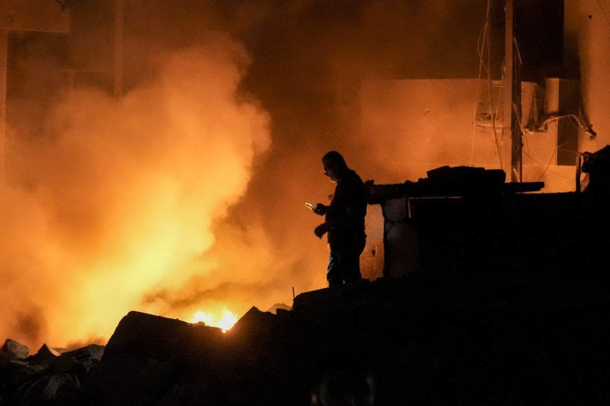 A man uses his mobile phone as flames and smoke rise at the scene of buildings hit by an Israeli airstrike in central Beirut, Lebanon, Thursday, Oct. 10, 2024. (AP Photo/Bilal Hussein)