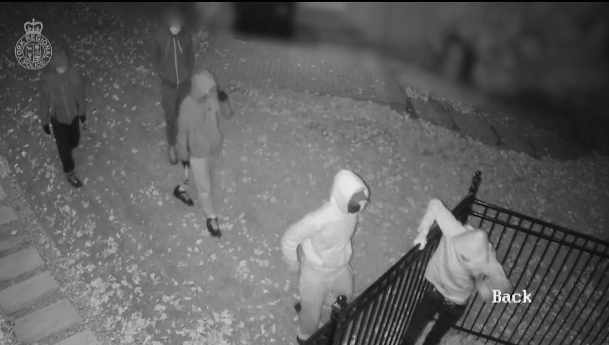 masked and hooded individuals hop a fence