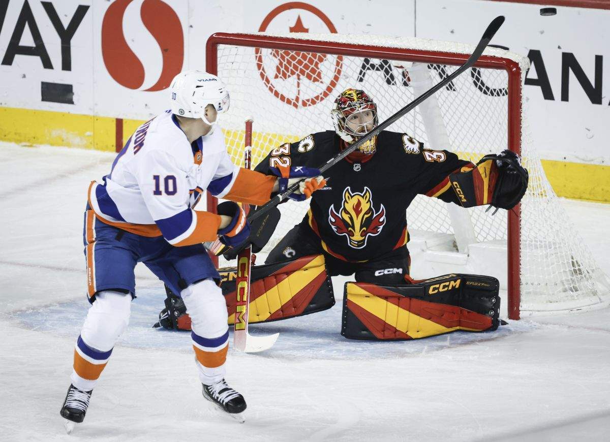 New York Islanders' Simon Holmstrom, left, tries to tip the puck past Calgary Flames goalie Dustin Wolf during first period NHL hockey action in Calgary, Alta., Tuesday, Nov. 19, 2024.