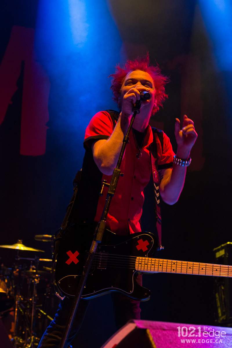 Deryck Whibley stands on stage singing into a microphone.