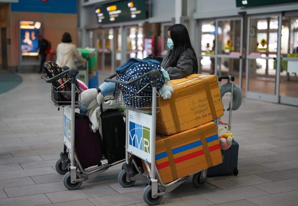 A passenger who arrived on a Cathay Pacific flight from Hong Kong stands with baggage on carts while waiting for other family members at Vancouver International Airport, in Richmond, B.C., on Jan. 4, 2023.