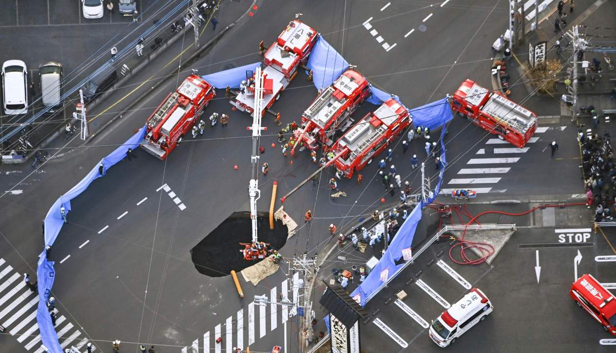First responders try to rescue the driver of a truck that fell into a sinkhole on a street in Yashio, northeast of Tokyo, Tuesday, Jan. 28, 2025.