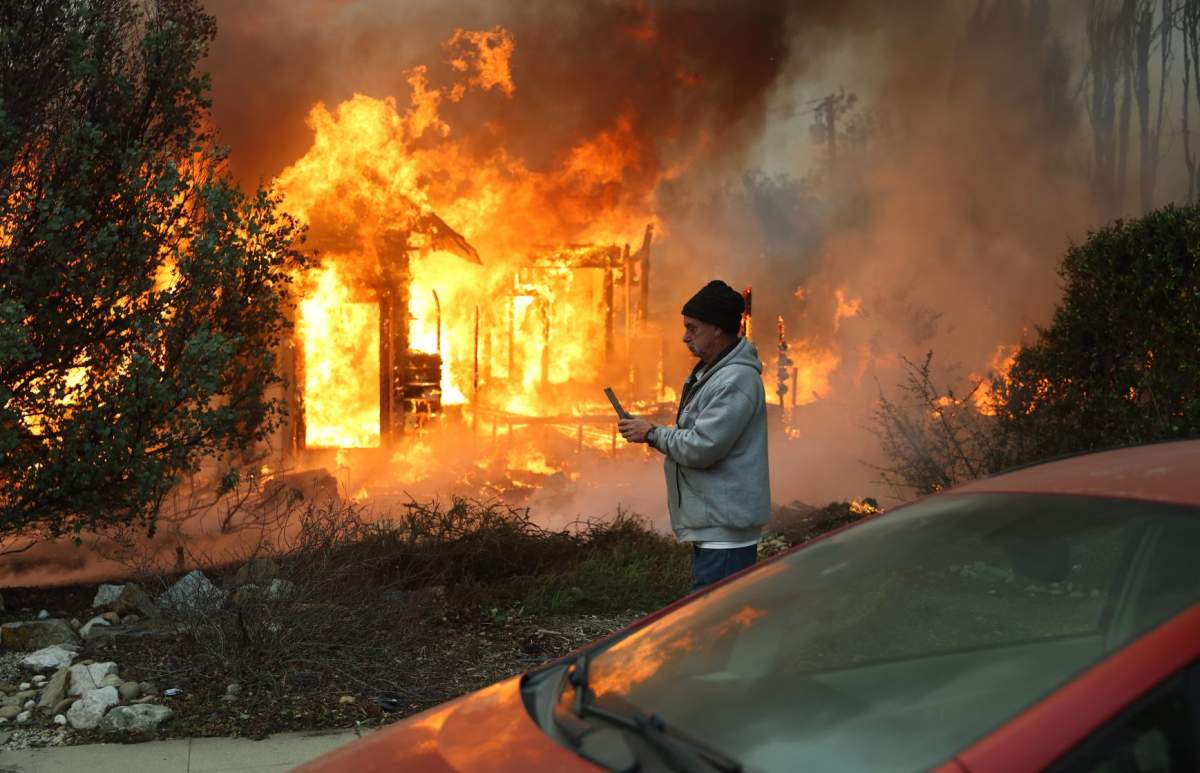 ALTADENA, CALIFORNIA - JANUARY 08: A person walks past a home burning during the Eaton Fire on January 8, 2025 in Altadena, California. Over 1,000 structures have burned, with two people dead, in wildfires fueled by intense Santa Ana Winds across L.A. County. (Photo by Mario Tama/Getty Images)