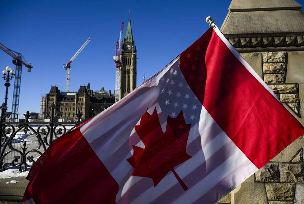 <p>A protester holds the flags of Canada and the United States outside on Parliament Hill in Ottawa, on Saturday, Feb. 1, 2025. THE CANADIAN PRESS/Justin Tang</p>.