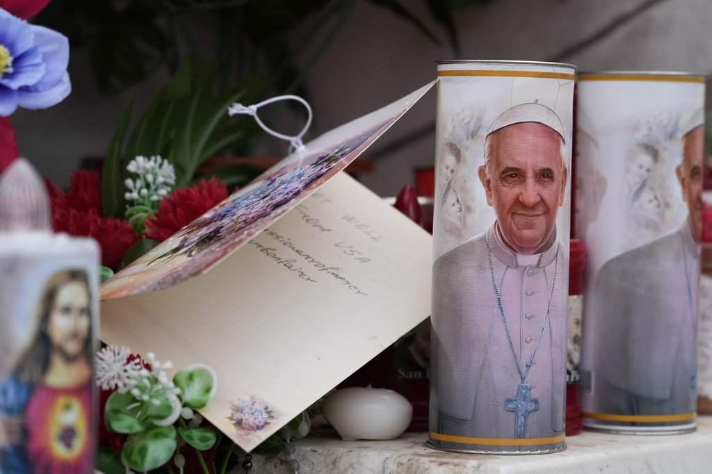 Candles with the pictures of Pope Francis are the laid under the statue of late Pope John Paul II outside Agostino Gemelli Polyclinic in Rome, Wednesday, Feb. 19, 2025, where the Pontiff is hospitalized since Friday, Feb. 14.