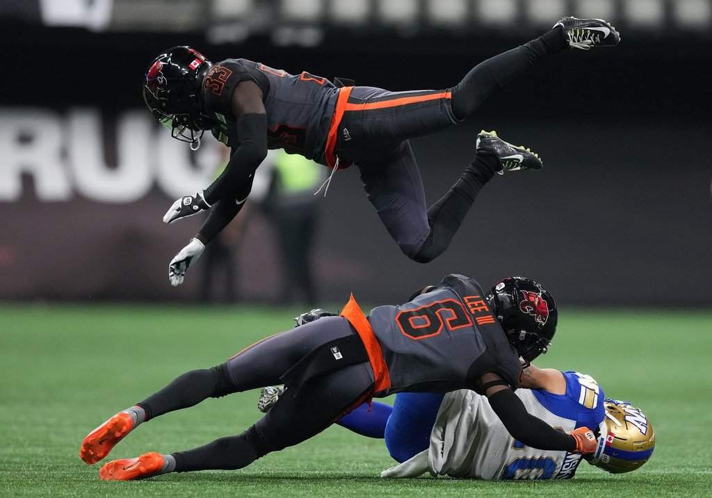 B.C. Lions' Emmanuel Rugamba (33) leaps over T.J. Lee (6) to avoid colliding with him as he tackles Winnipeg Blue Bombers' Nic Demski, bottom, during the first half of CFL football game in Vancouver, on Saturday, Oct. 15, 2022. Rugamba embraces the challenge of helping return the Edmonton Elks to the CFL playoffs.