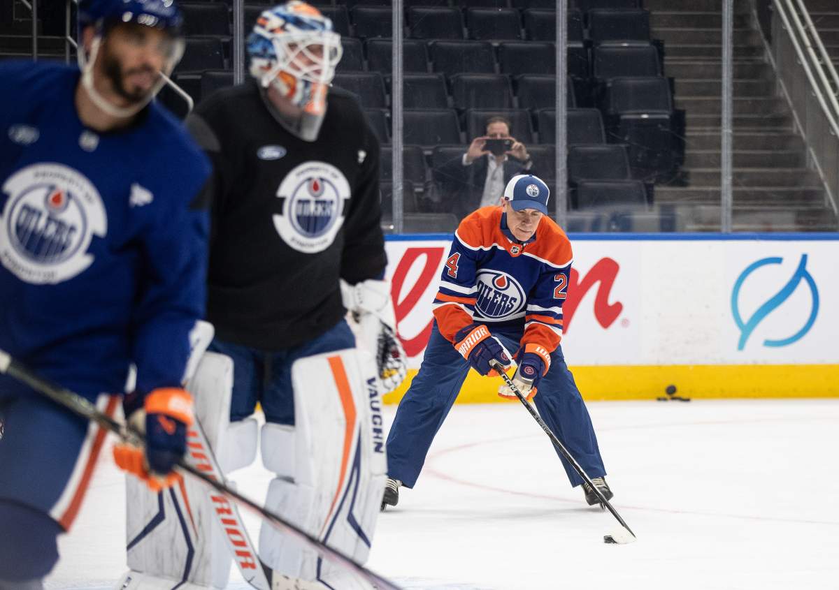 Prime Minister Mark Carney wears an orange and blue Oilers uniform while on the ice playing hockey.
