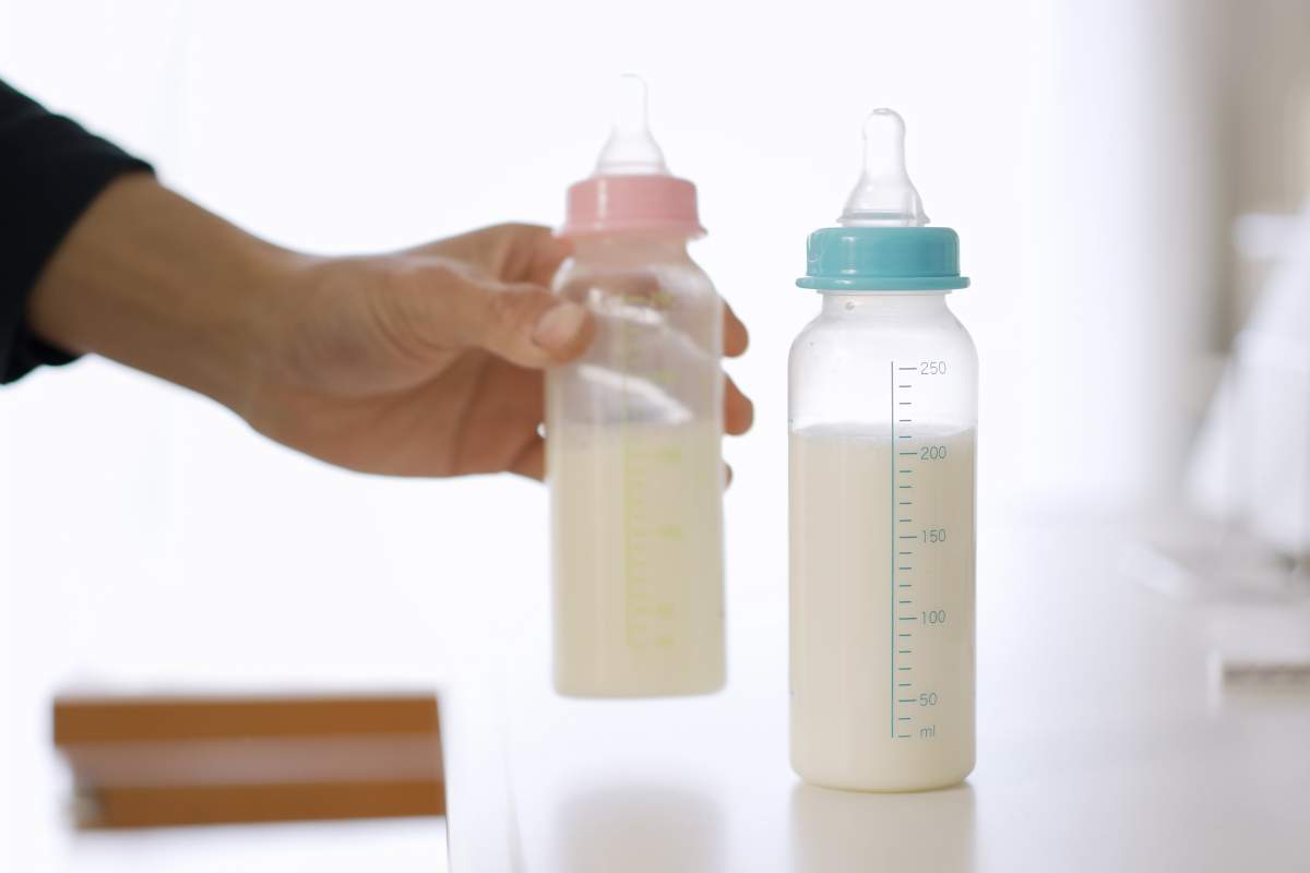 A hand is visible reaching for two baby bottles of milk.