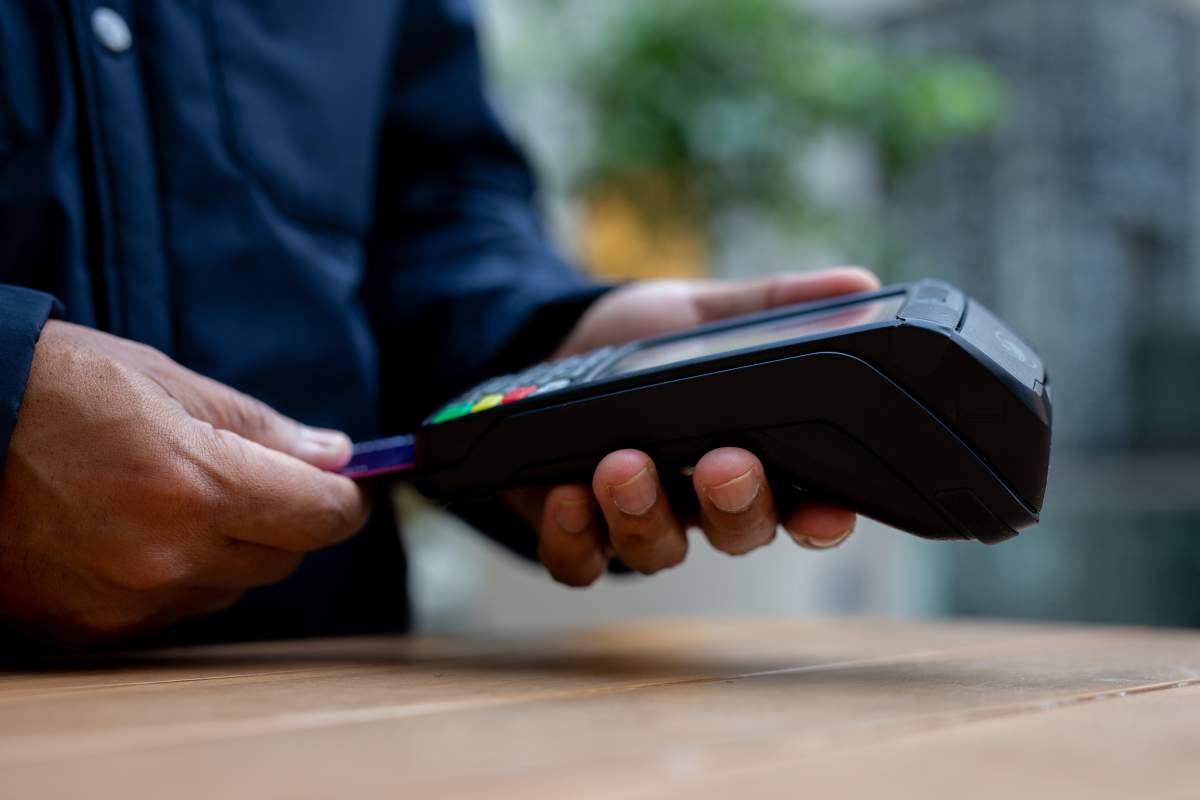 Customer is holding a credit card and inserting it into a dataphone to make a contactless payment