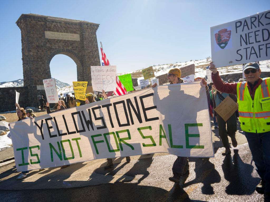 Protesters hold signs at Roosevelt Arch, the northern entrance to Yellowstone Park on March 1, 2025 in Gardiner, Montana.