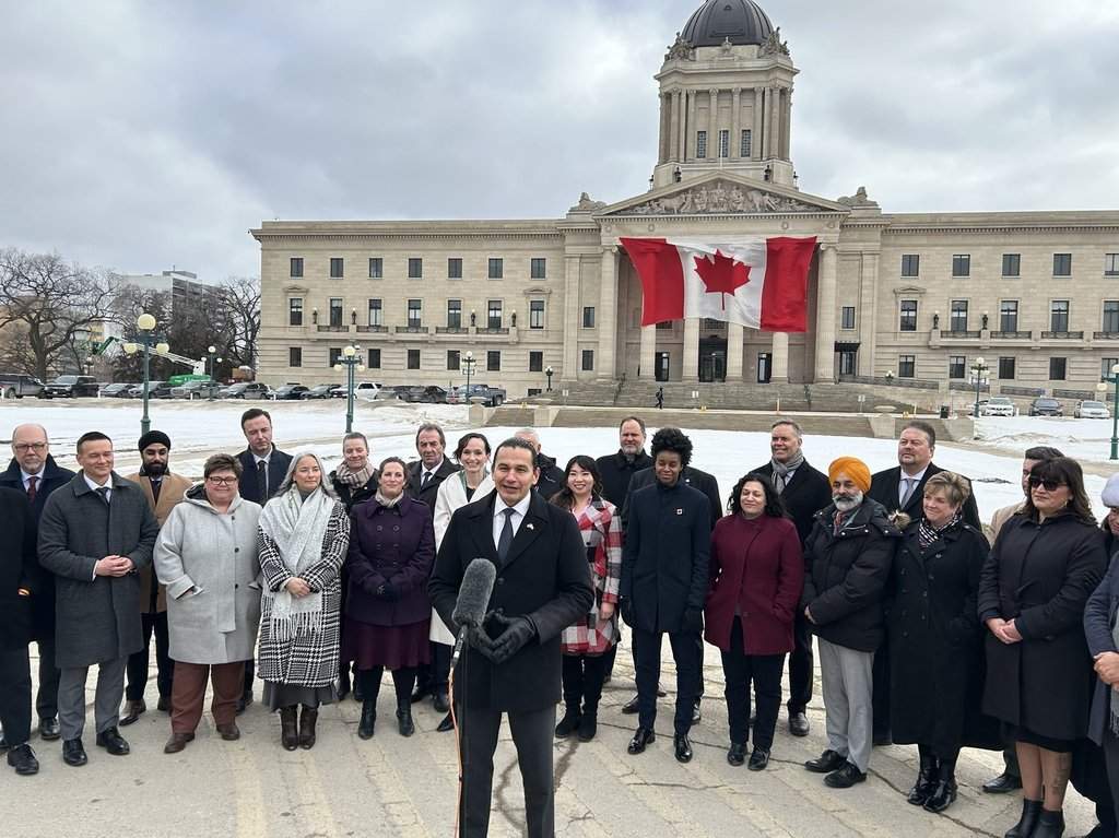 Premier Wab Kinew and members of his NDP caucus stand outside the legislative building for a press conference in Winnipeg on Tuesday, March 4, 2025. Politicians are returning to the Manitoba legislative chamber today amid the economic fallout from U.S. tariffs and ongoing challenges in provincial health care. 