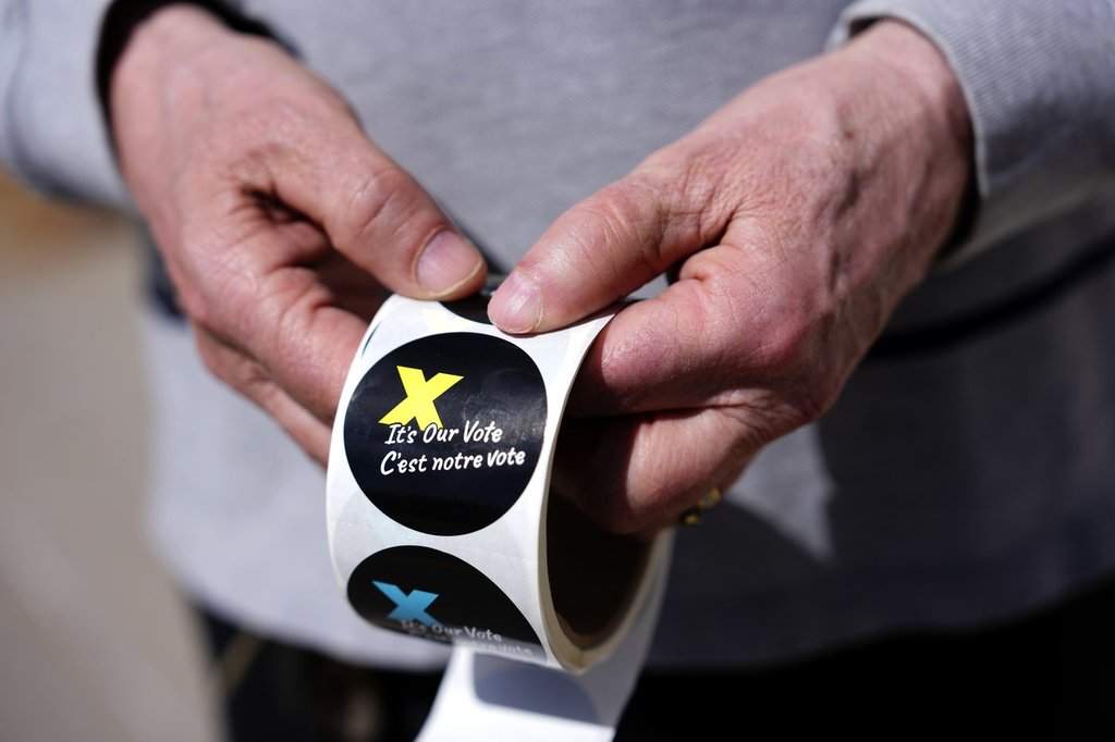 A voting information officer holds stickers to be given to voters after casting their ballots, outside a polling location in Ottawa.