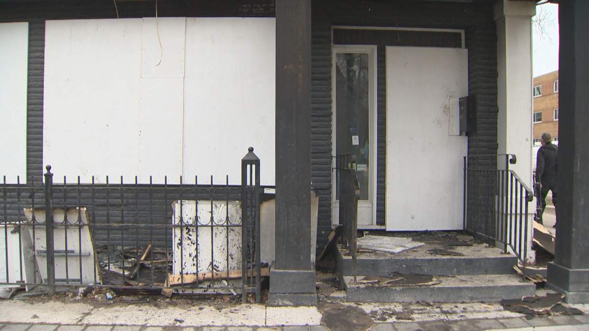 A boarded up storefront with charred pieces of debris strewn in front of the door.