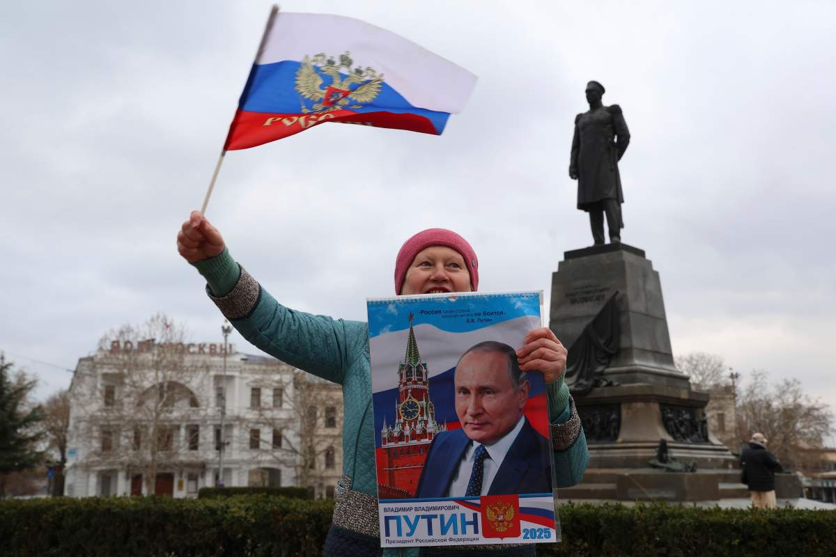 A woman holds a portrait of Russian President Vladimir Putin as she waves a Russian national flag, as other gather to mark the 11-year anniversary of Crimea's annexation by Russia in Sevastopol, Crimea, Tuesday, March 18, 2025.