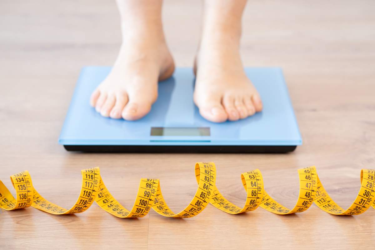 Tape measure and woman feet standing on weigh scales.Diet, weight loss and feet of a woman on a scale for body check, measure and balance to lose weight on the floor. Obesity, scales and girl with tape