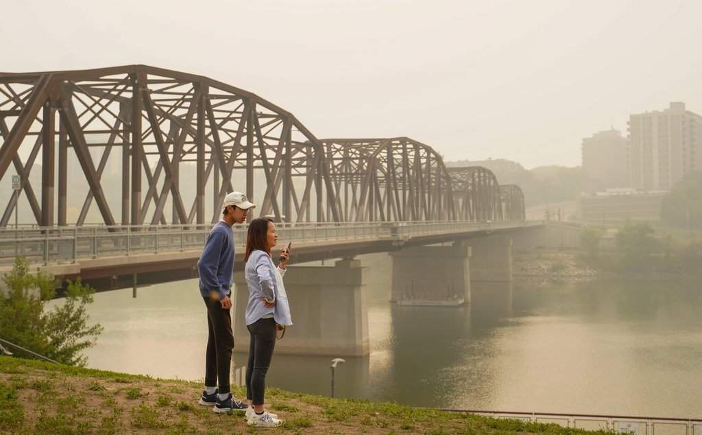 Two people stand as the South Saskatchewan River is enveloped by forest fire smoke in Saskatoon, on Sunday, Sept. 3, 2023. Saskatchewan public safety officials say they are anticipating an average wildfire season with a cooler spring and hotter summer.