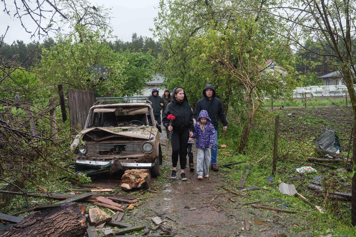 People carry flowers to the rubble of a destroyed house where three children were killed by a Russian strike in Korostyshiv, Ukraine, May 25, 2025. (AP Photo/Evgeniy Maloletka).