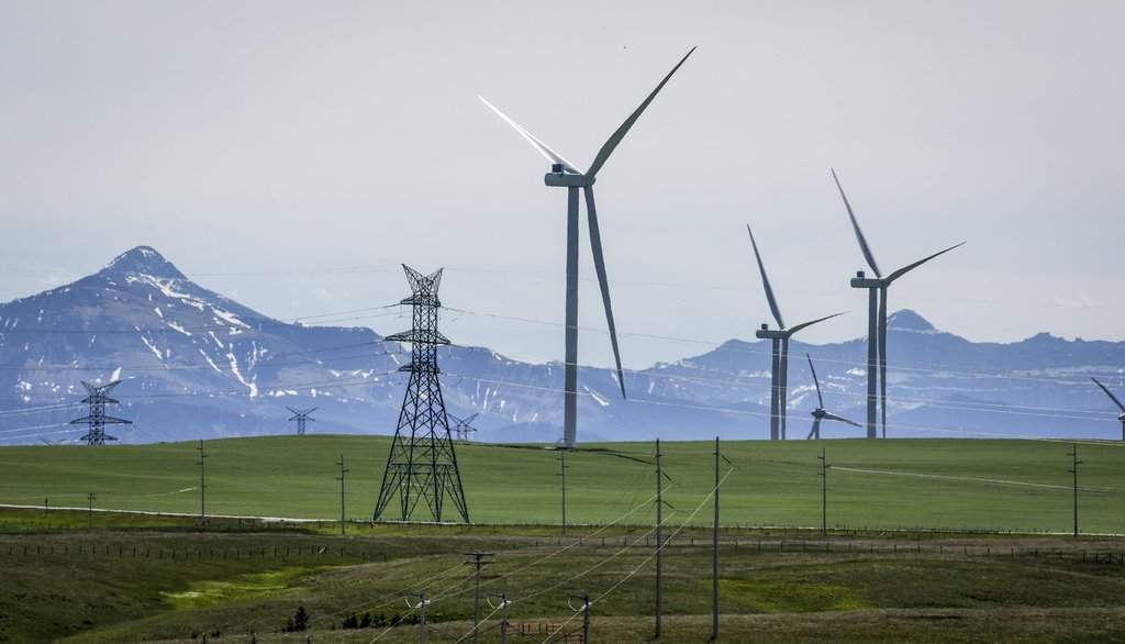 Power transmission lines and wind turbines as seen with the Rocky Mountains in the background near Pincher Creek, Alta., Thursday, June 6, 2024.