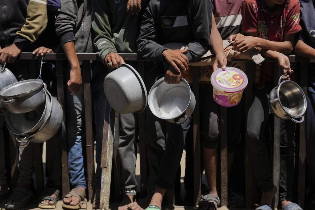 Holding their pots, Palestinians wait to get donated food at a community kitchen in Khan Younis, southern Gaza Strip, Monday, June 2, 2025.