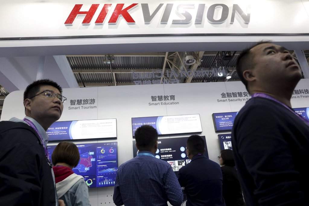 In this Tuesday, Oct. 23, 2018, file photo, visitors pass by a booth for state-owned surveillance equipment manufacturer Hikvision at the Security China 2018 expo in Beijing, China. (AP Photo/Ng Han Guan, File).