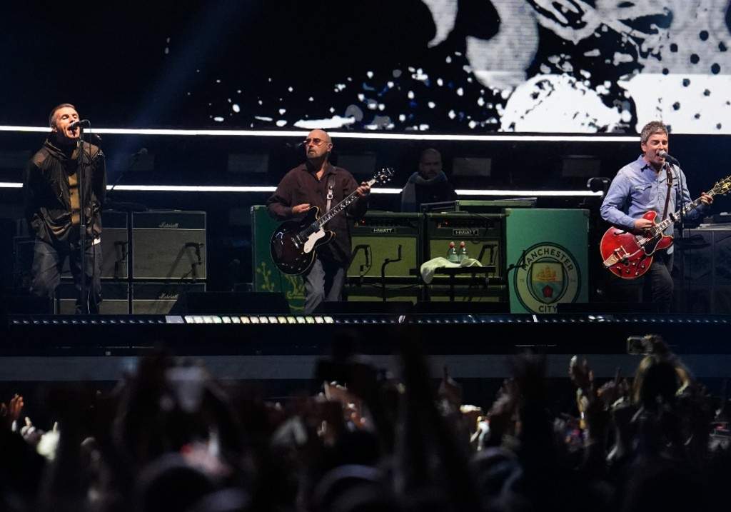(L-R) Liam Gallagher, lead singer, Paul Arthurs, guitarist and Noel Gallagher, singer and guitarist of British rock band Oasis perform on stage at the Principality Stadium in Cardiff on July 4, 2025.