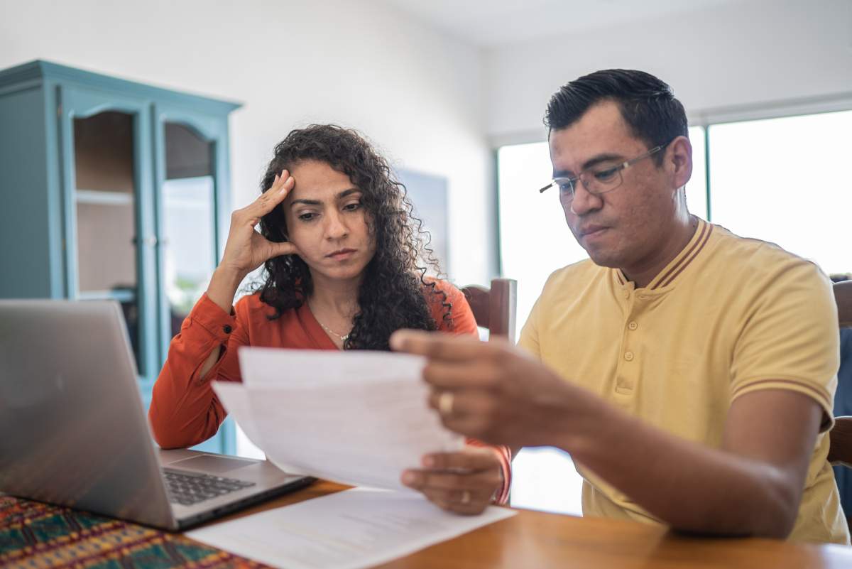 A couple reads a troubling letter while sitting in front of a laptop.