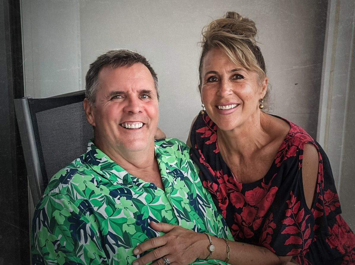 Photo of Carol Messenger in dress and husband Dan in tropical green shirt, both smiling.