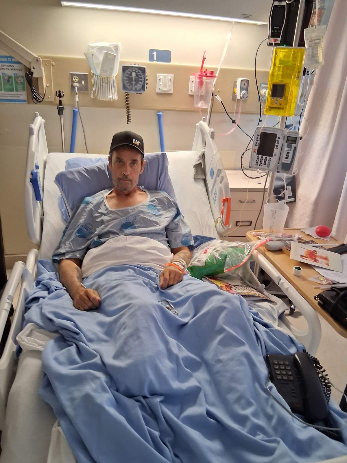 A man in a hat sits in a hospital bed.