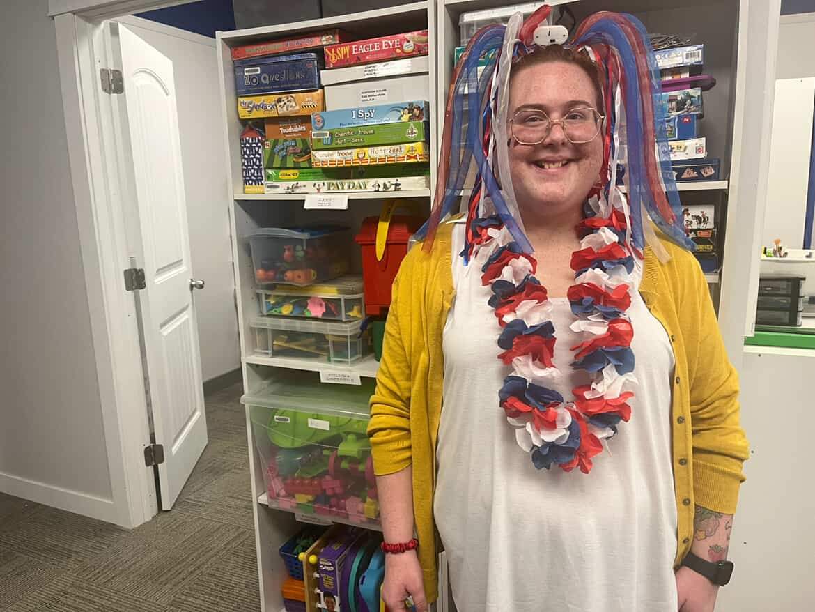 A woman wearing accessories in Acadian colours smiles in front of shelves full of board games.