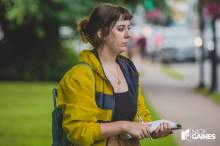 A female reporter with brown hair wearing a yellow jacket and holding a note pad.