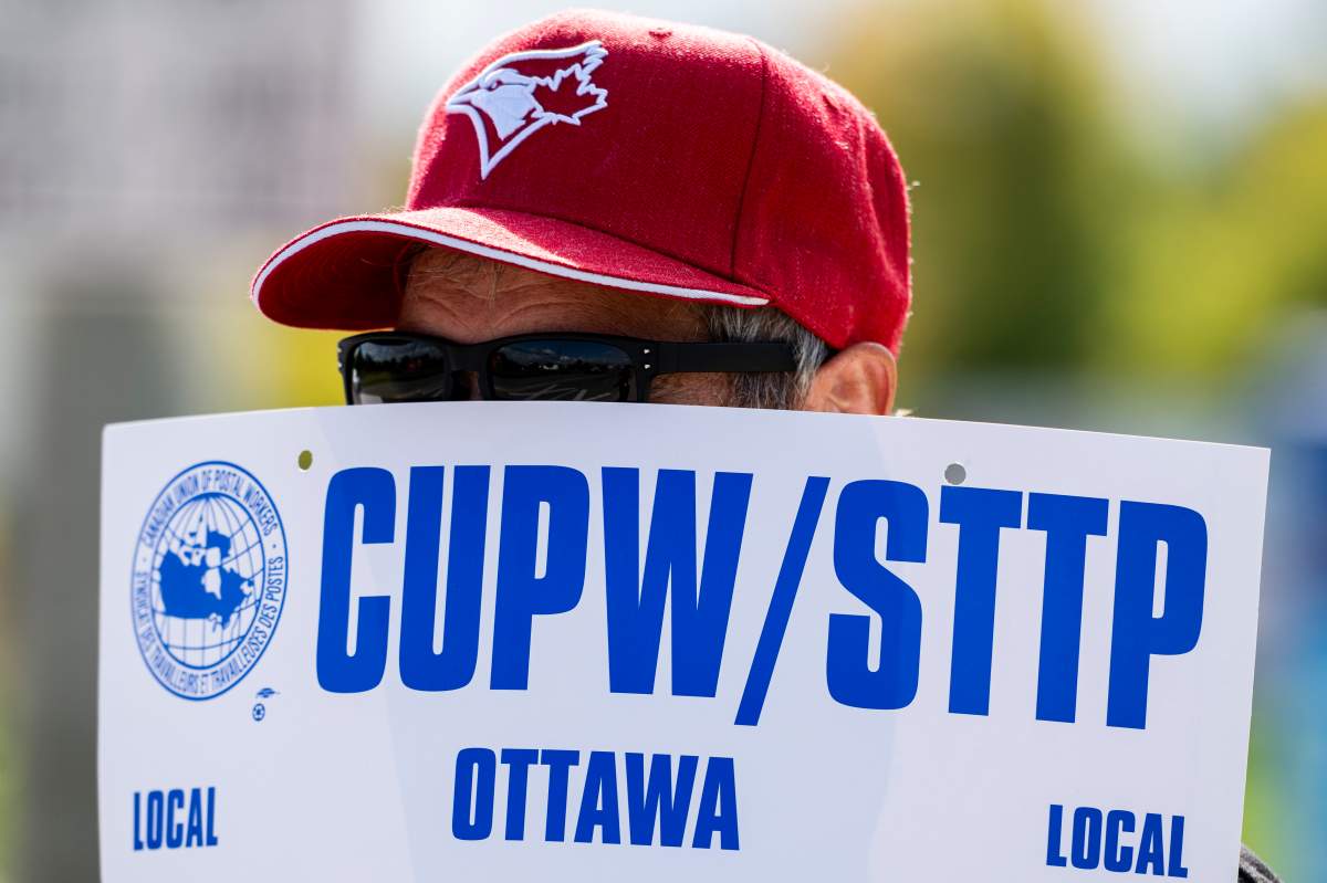 A Canada Post worker holds a Canadian Union of Postal Worker (CUPW) sign outside a Canada Post depot in Ottawa, on Friday, Sept. 26, 2025.