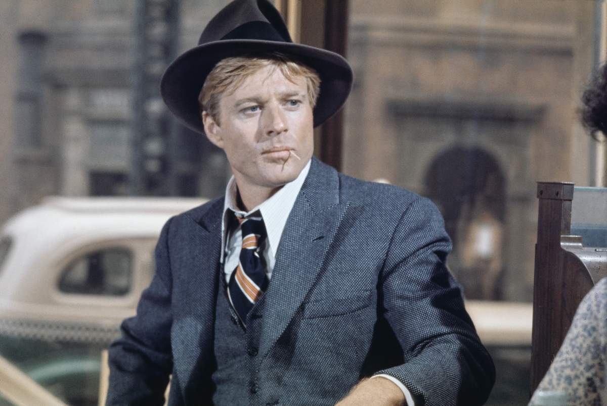 American actor Robert Redford wearing a grey tweed blazer over a matching waistcoat and a white shirt, with a diagonally striped tie, with a grey fedora, in a scene from 'The Sting', filmed in the United States, 1973. The crime caper directed by George Roy Hill, starred Redford as Johnny Hooker.