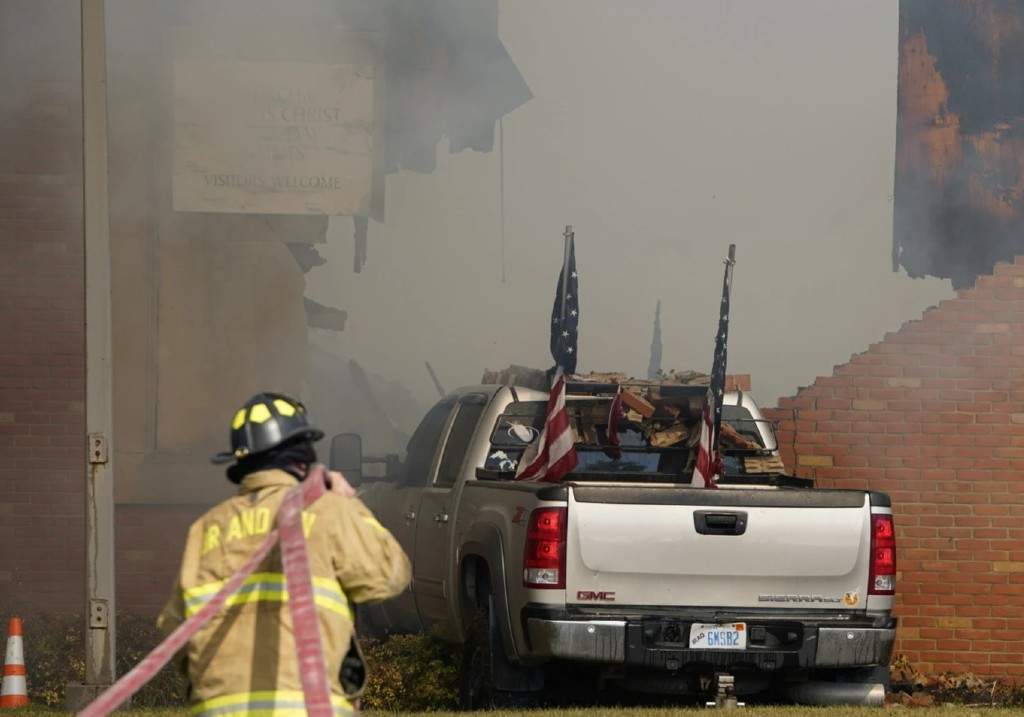 A vehicle that was rammed into the building is surrounded by smoke as a firefighter works on the scene at the Church of Jesus Christ of Latter-day Saints in Grand Blanc, Mich., Sunday, Sept. 28, 2025.