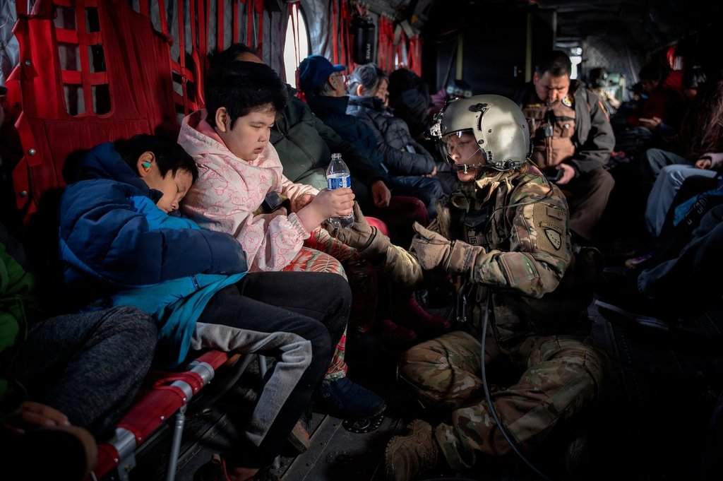 In this photo provided by the Alaska Army National, Guard Sgt. Mary Miller, a helicopter crew chief, passes a bottle of water to a child while evacuating displaced people from Kwigillingok, Alaska, during recovery operations on Thursday, Oct. 16, 2025. (Joseph Moon/Alaska National Guard via AP)
