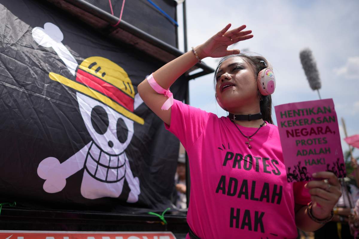 An activists holds a poster as a flag bearing an image of skull with straw hat from the popular Japanese anime One Piece is displayed, during a rally denouncing violence allegedly committed by the police in days of protests against lavish allowances given to the members of the parliament, in Jakarta, Indonesia, Wednesday, Sept. 3, 2025. (AP Photo/Dita Alangkara)