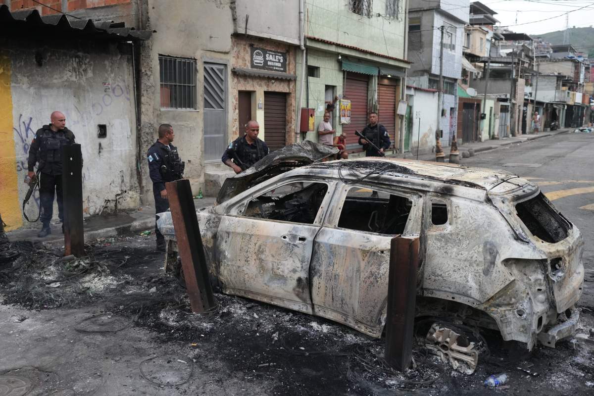 Police look at a burned car used by alleged drug traffickers as a roadblock during a police operation in the Complexo do Alemao favela where the criminal organization "Comando Vermelho" operates in Rio de Janeiro, Tuesday, Oct. 28, 2025.