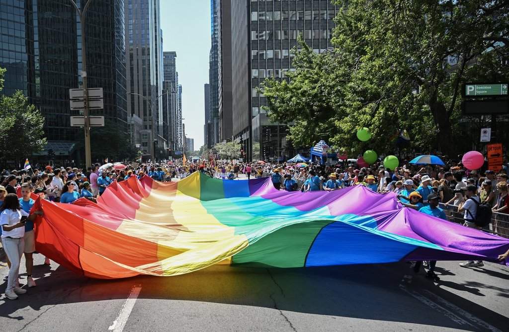 Participants carry a rainbow flag along a street during the Pride parade in Montreal, Sunday, August 10, 2025.