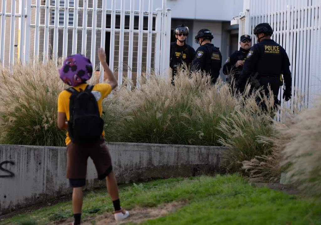 A protester waves to Department of Homeland Security officials as they walk to the gates of the U.S. Immigration and Customs Enforcement facility after inspecting an area outside on Sunday, Sept. 28, 2025, in Portland, Ore.