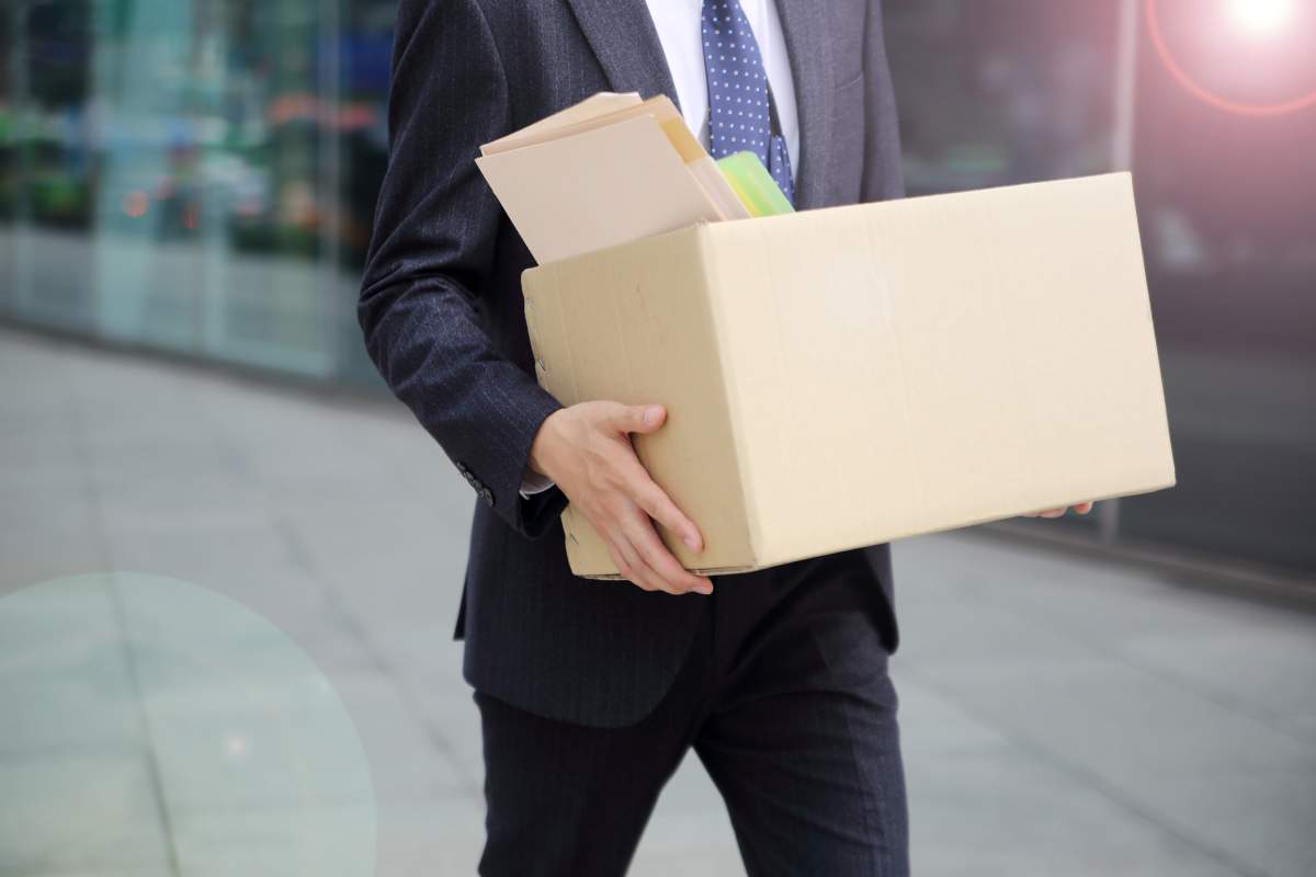 A businessman carries his office supplies in a cardboard box.