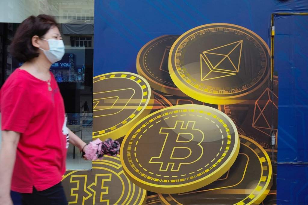 In this June 1, 2021, file photo, a woman walks past an advertisement for the Bitcoin cryptocurrency in Hong Kong. (AP Photo/Vincent Yu, File).