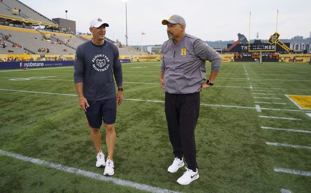 Montreal Alouettes Head Coach Jason Maas, left, chats with Hamilton Tiger Cats Head Coach and Offensive Coordinator Scott Milanovich before the start of CFL football game action in Hamilton, Ont. on Friday, June 27, 2025. THE CANADIAN PRESS/Peter Power.