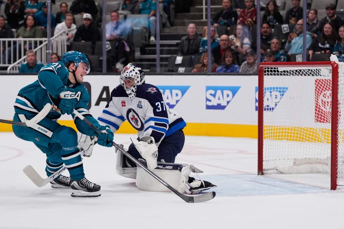 San Jose Sharks center Macklin Celebrini, left, shoots in front of Winnipeg Jets goaltender Connor Hellebuyck (37) during the first period of an NHL hockey game, Friday, Nov. 7, 2025, in San Jose, Calif. (AP Photo/Godofredo A. Vásquez).