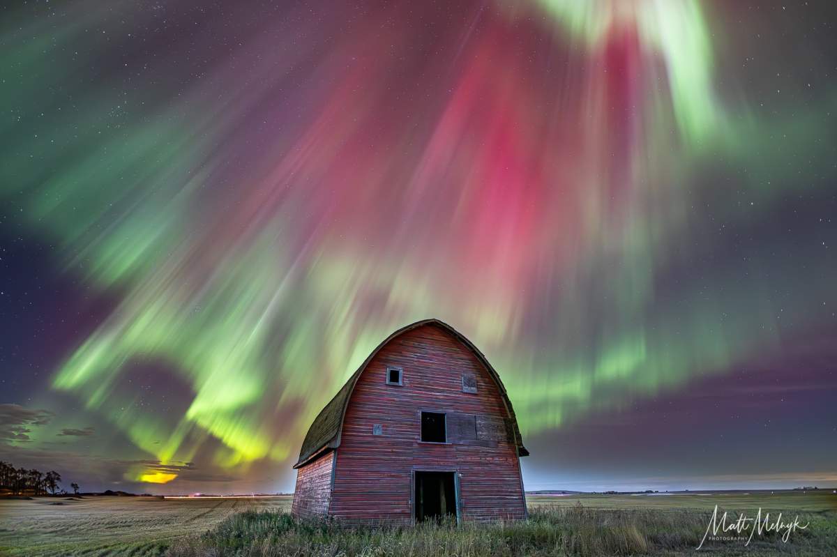 Aurora borealis shines behind a barn.