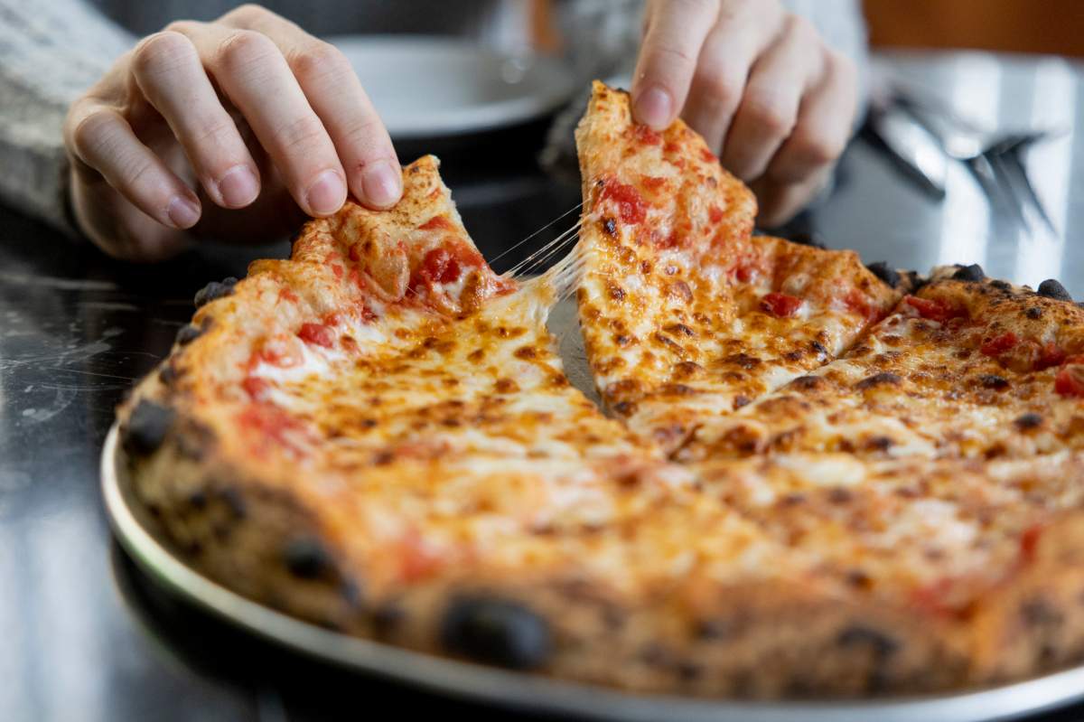 A person takes a slice of pizza. 