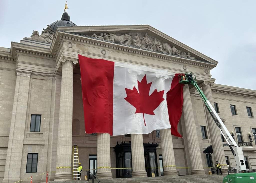 Workers install a large Canadian flag on the front of the Manitoba legislative building in Winnipeg on Tuesday Mar. 4, 2025. THE CANADIAN PRESS/Steve Lambert.