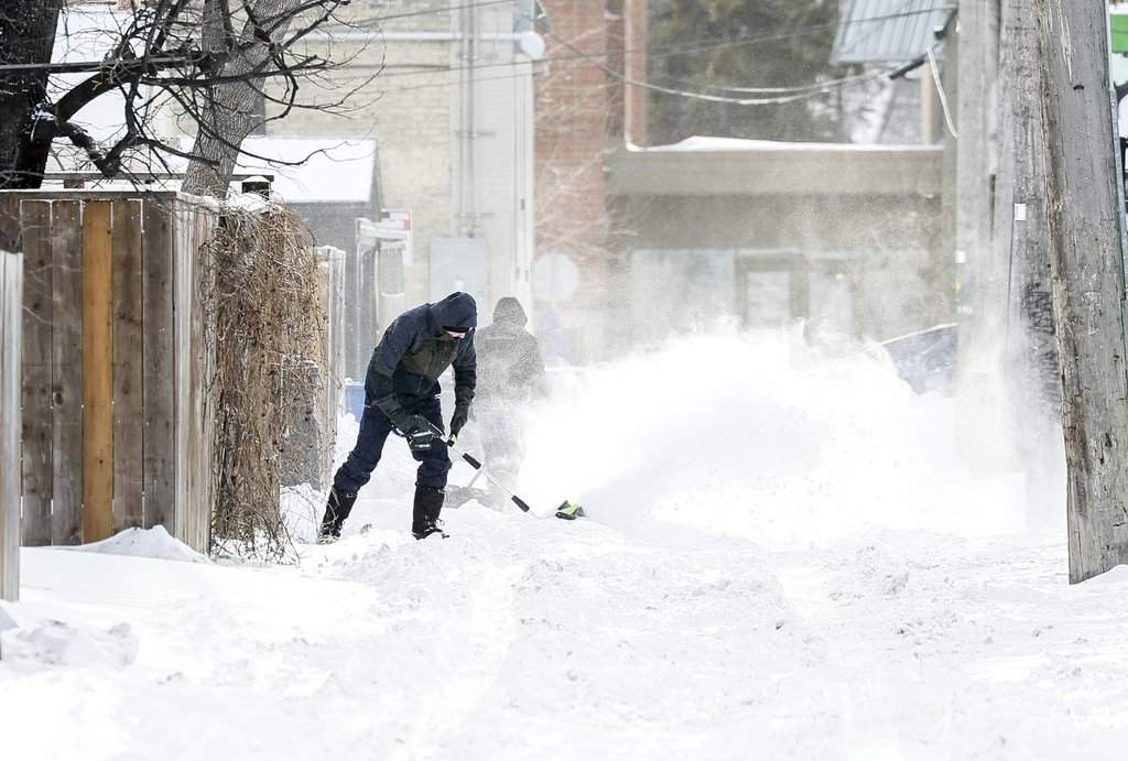 People clear snow after an overnight storm, in Winnipeg, Thursday, Dec. 18, 2025.