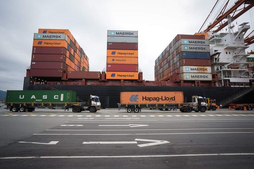 Transport trucks carry cargo containers to be loaded on the Hapag-Lloyd container ship Frankfurt Express at the DP World Centerm terminal at port, in Vancouver, on Sunday, Aug. 3, 2025. THE CANADIAN PRESS/Darryl Dyck.