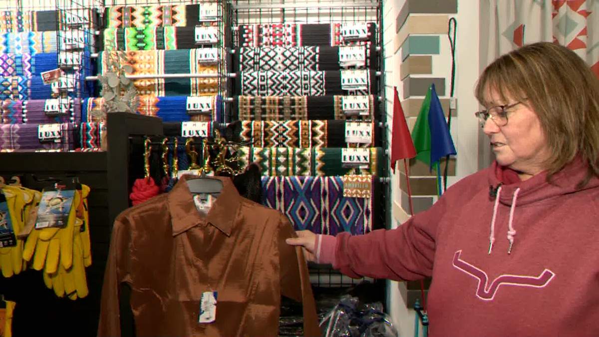 Beth Latwaitis, owner of Ranch by Design, shows off a shirt similar to one she recently sold to an American customer, but is now stuck in tariff limbo between Canada and the U.S.