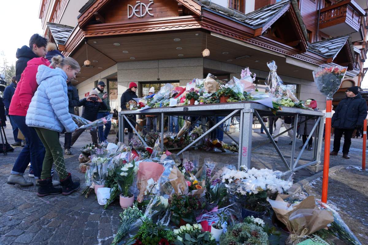 People bring flowers and letters near the sealed off Le Constellation bar, where a devastating fire left dead and injured during the New Year's celebrations in Crans-Montana, Swiss Alps, Switzerland, Friday, Jan. 2, 2026.